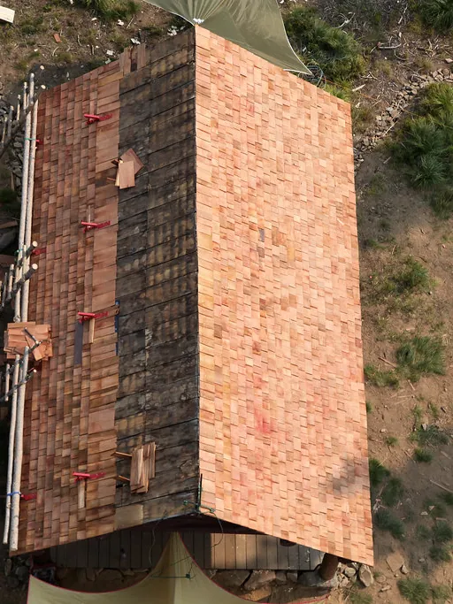 A crew laying new asphalt shingles on a house roof, seen from above